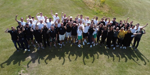 The group of golfers crowded together on the golf course cheering to the camera
